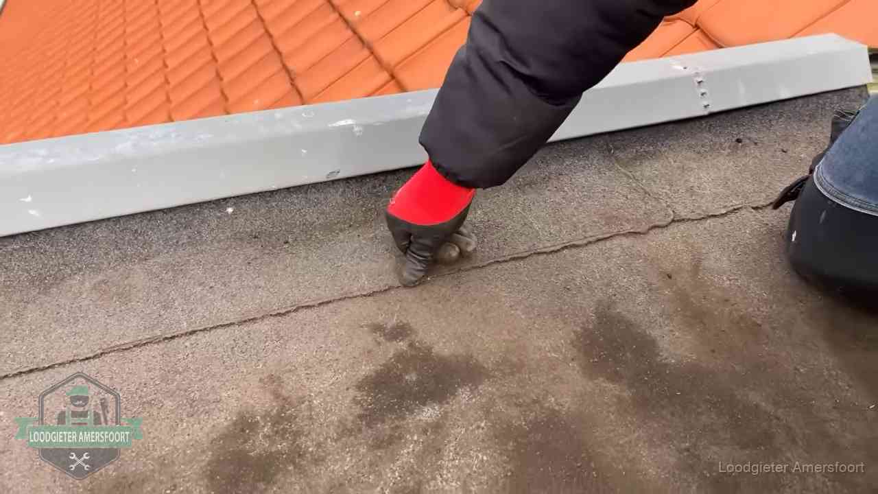 Vakman wijst een naad met vochtplekken aan op een bitumen plat dak in Amersfoort