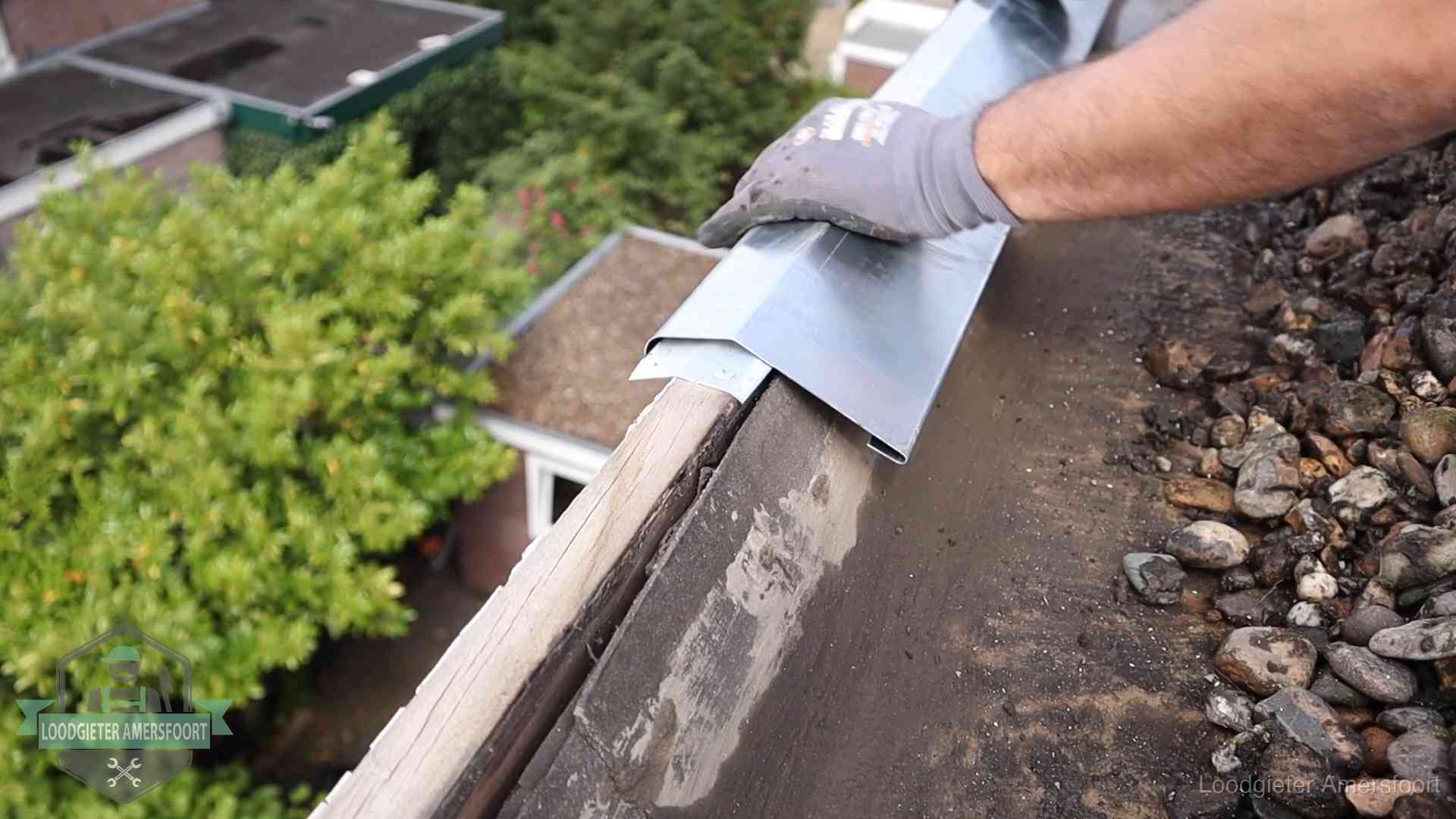 Dakdekker plaatst een zinken deklijst op een dakrand met uitzicht over een woonwijk in Amersfoort