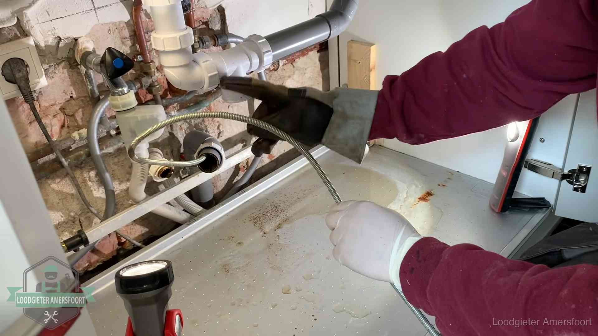 Ontstoppingsveer gaat in een geopende sifonaansluiting onder het aanrecht in Amersfoort