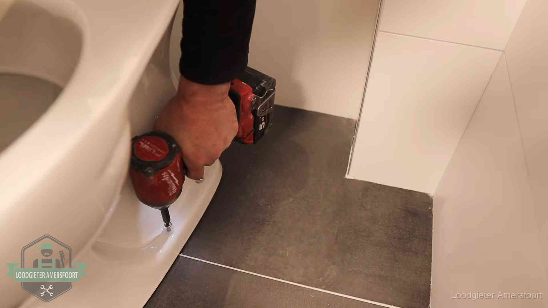 Loodgieter zet de voet van een wc-pot vast op de tegelvloer in Amersfoort